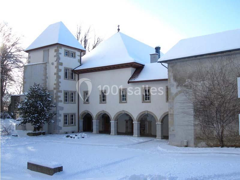 Bâtiment historique avec arcades et toit enneigé, entouré d'arbres en hiver.