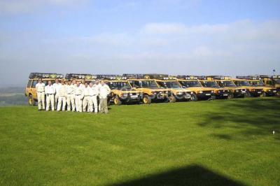 Un grand groupe de personnes en t-shirts verts pose joyeusement devant des véhicules stationnés en extérieur.