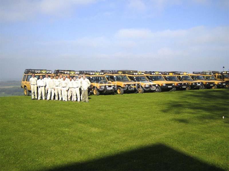 Un groupe de personnes en tenue claire pose devant une rangée de véhicules tout-terrain jaunes alignés sur une pelouse.