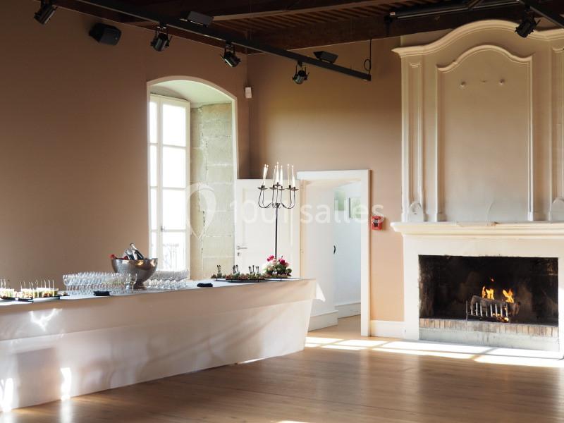 Salle lumineuse avec cheminée allumée, table dressée pour un buffet et chandelier décoratif.