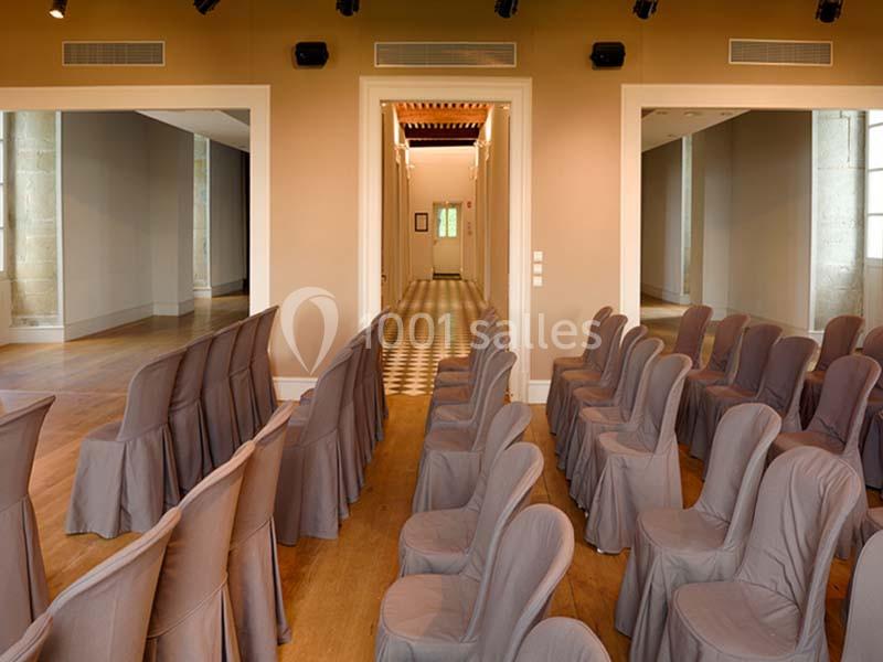 Salle de réunion lumineuse avec des rangées de chaises recouvertes de housses grises et un couloir central.