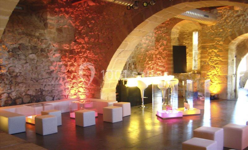 Salle en pierre avec éclairage coloré, mobilier moderne blanc et bar lumineux dans un cadre chaleureux.