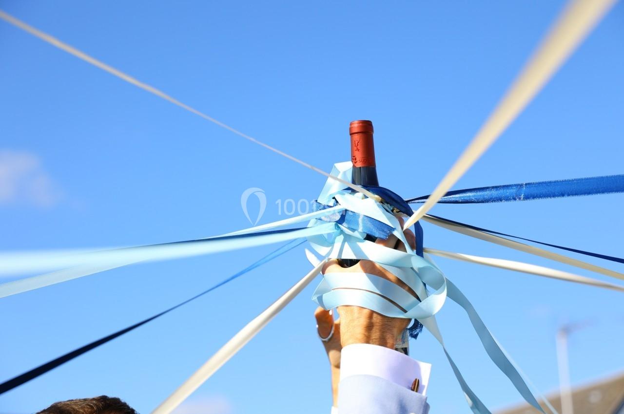 Main tenant une bouteille de vin entourée de rubans colorés tendus vers le ciel bleu.