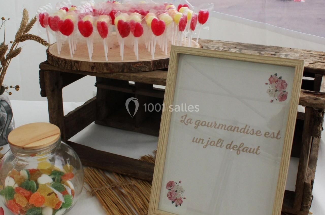 Bonbonnière et sucettes colorées sur une table décorée, avec un cadre affichant ’La gourmandise est un joli défaut’.
