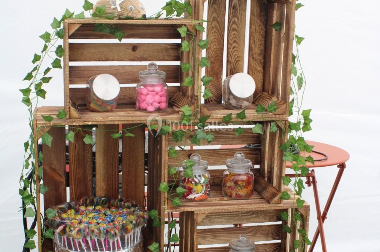 Casiers en bois empilés décorés de lierre, contenant des bocaux de bonbons colorés et un plateau de sucettes.