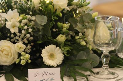 Table ronde élégamment dressée avec vaisselle, couverts, serviettes roses et centre de table floral coloré.