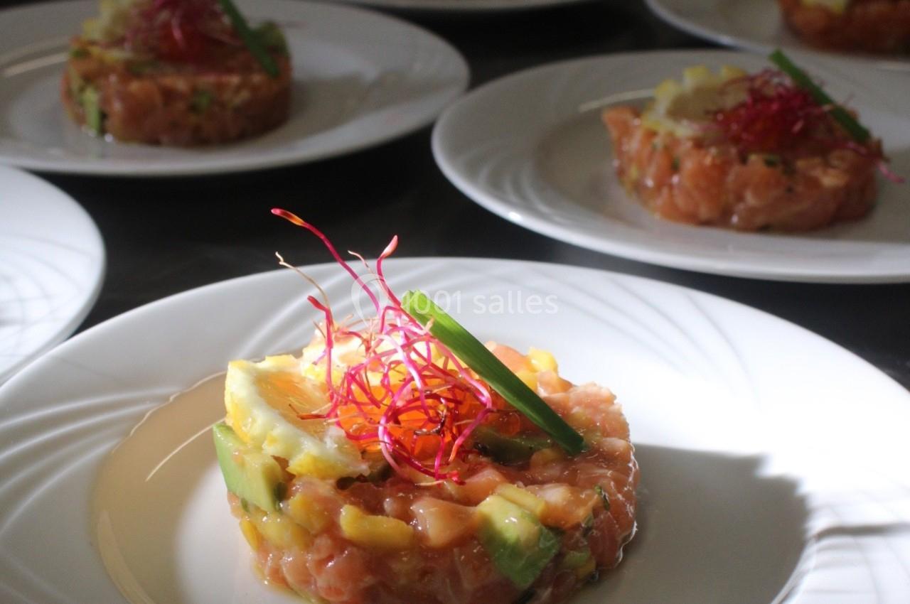 Tartare de saumon avec avocat, mangue et décoration de germes rouges, servi sur une assiette blanche.