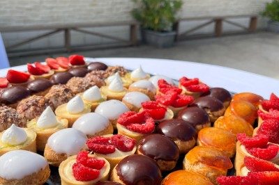 Table ronde élégamment dressée avec vaisselle, couverts, serviettes roses et centre de table floral coloré.