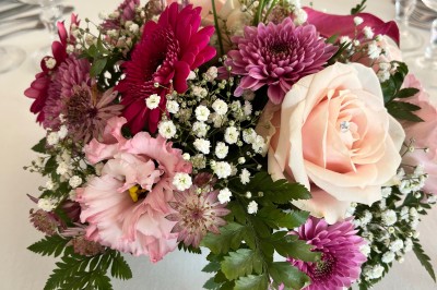 Table ronde élégamment dressée avec vaisselle, couverts, serviettes roses et centre de table floral coloré.