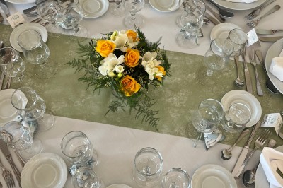 Table ronde élégamment dressée avec vaisselle, couverts, serviettes roses et centre de table floral coloré.