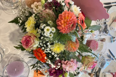 Table ronde élégamment dressée avec vaisselle, couverts, serviettes roses et centre de table floral coloré.