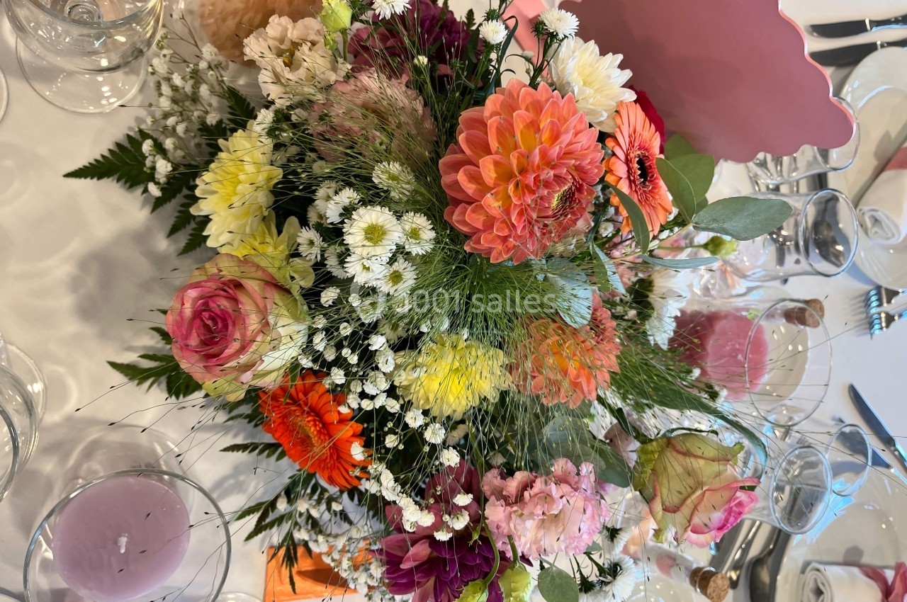 Bouquet coloré de fleurs variées, posé sur une table dressée avec verres et décorations.