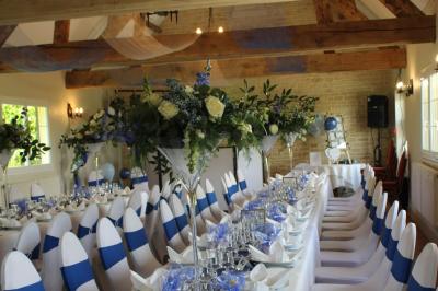 Table ronde élégamment dressée avec vaisselle, couverts, serviettes roses et centre de table floral coloré.