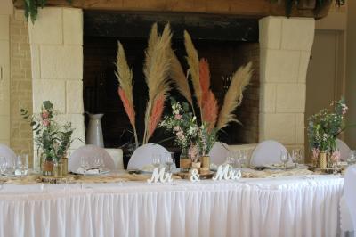 Table ronde élégamment dressée avec vaisselle, couverts, serviettes roses et centre de table floral coloré.