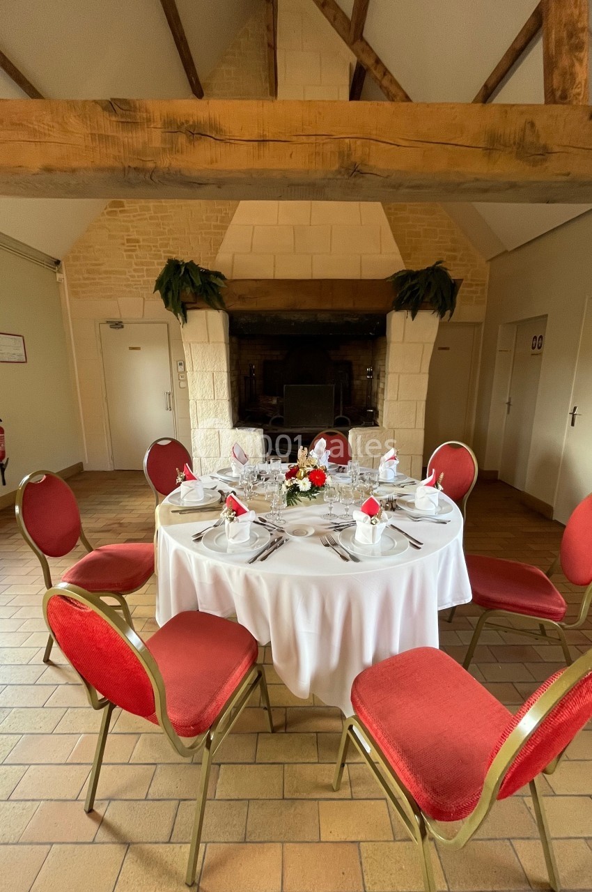 Table ronde dressée avec nappes blanches, vaisselle élégante et centre de table floral, entourée de chaises rouges.
