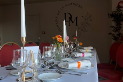 Table ronde élégamment dressée avec vaisselle, couverts, serviettes roses et centre de table floral coloré.