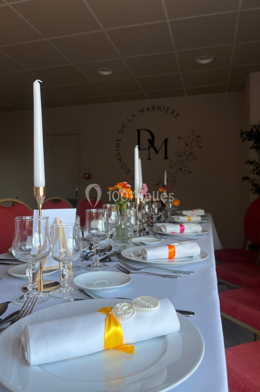 Table dressée élégamment avec vaisselle blanche, bougies, verres et décorations florales colorées dans une salle sobre.