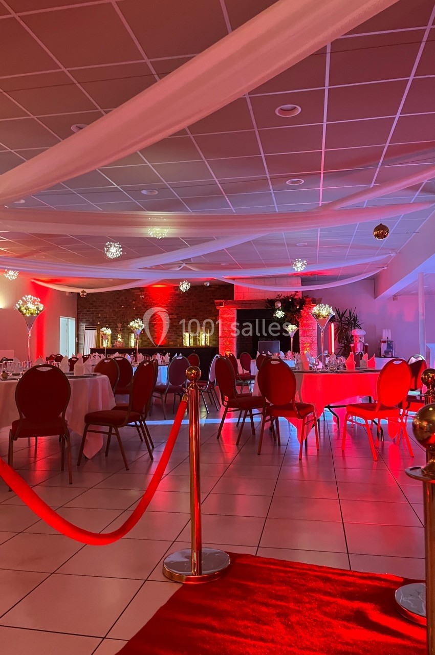 Salle de réception décorée avec des tables rondes, des chaises rouges et un éclairage d'ambiance rouge et blanc.