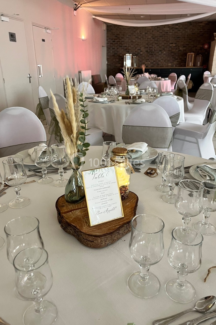 Salle de réception décorée avec des tables rondes, nappes blanches, centres de table naturels et vaisselle élégante.