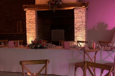 Table ronde élégamment dressée avec vaisselle, couverts, serviettes roses et centre de table floral coloré.