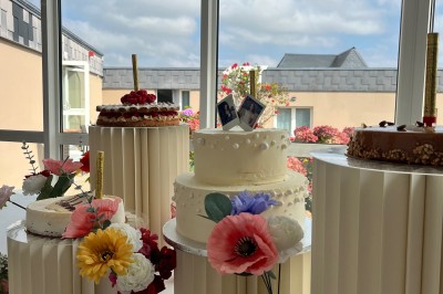 Table ronde élégamment dressée avec vaisselle, couverts, serviettes roses et centre de table floral coloré.