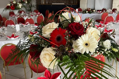 Table ronde élégamment dressée avec vaisselle, couverts, serviettes roses et centre de table floral coloré.