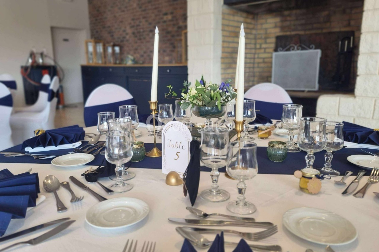 Table dressée pour un repas élégant avec nappes blanches, serviettes bleues, bougies et centre de table floral.