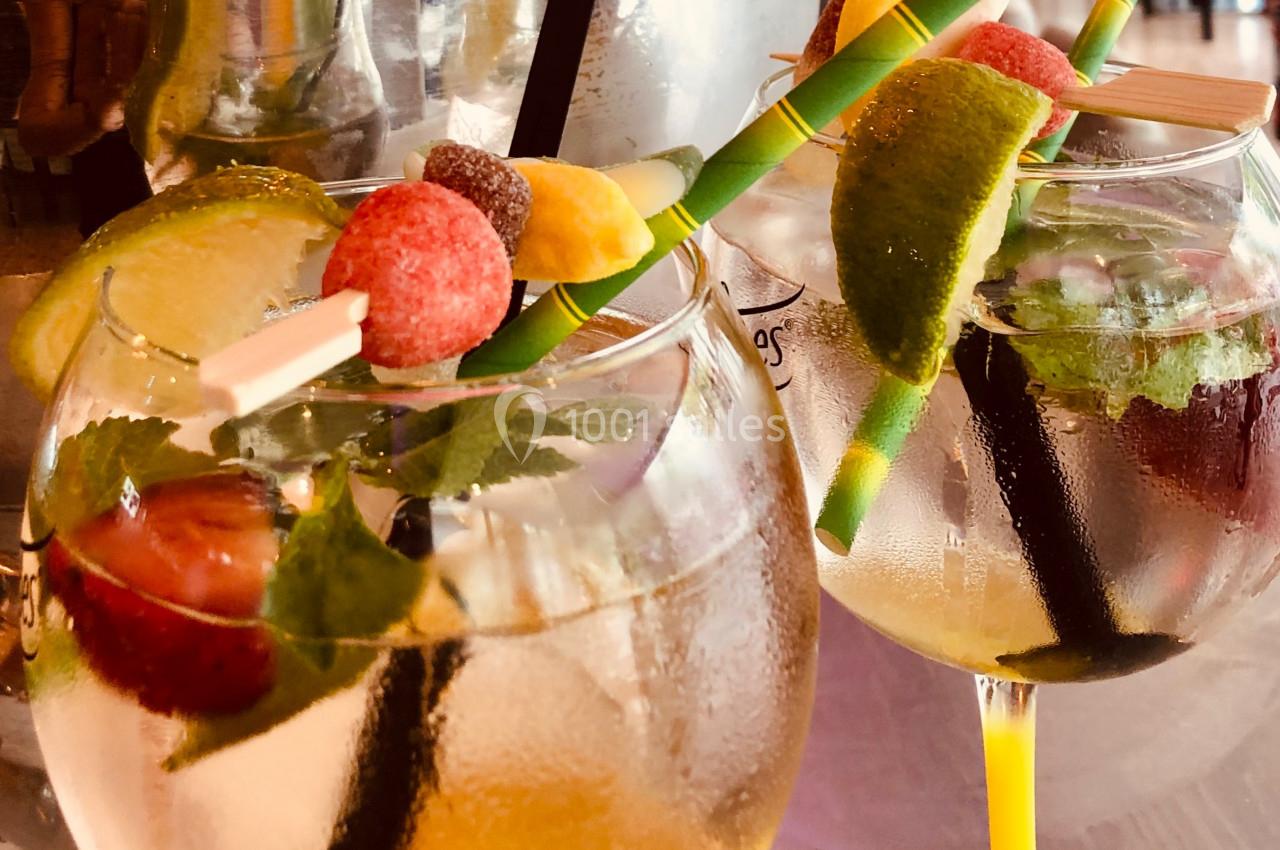 Deux verres de cocktail garnis de fruits frais, glaçons, feuilles de menthe et pailles colorées.