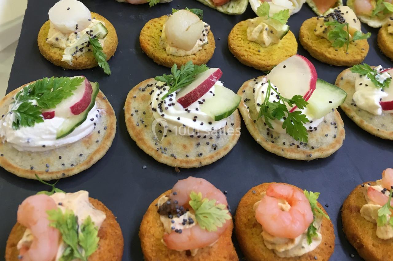 Assortiment de canapés variés garnis de crevettes, légumes frais, fromage et herbes sur un plateau noir.