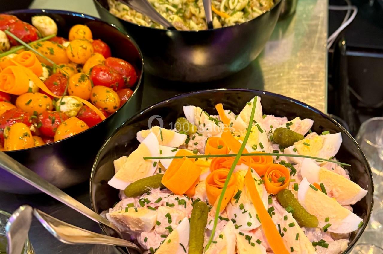 Assortiment de salades dans des bols noirs : salade de pommes de terre, tomates cerises et pâtes au pesto.