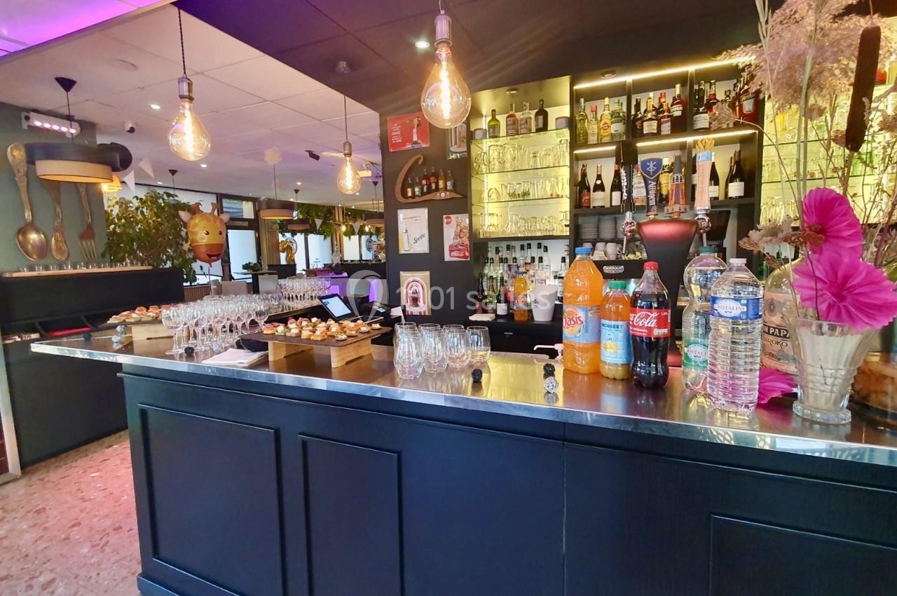 Comptoir de bar avec boissons, verres, amuse-bouches et étagères remplies de bouteilles en arrière-plan.