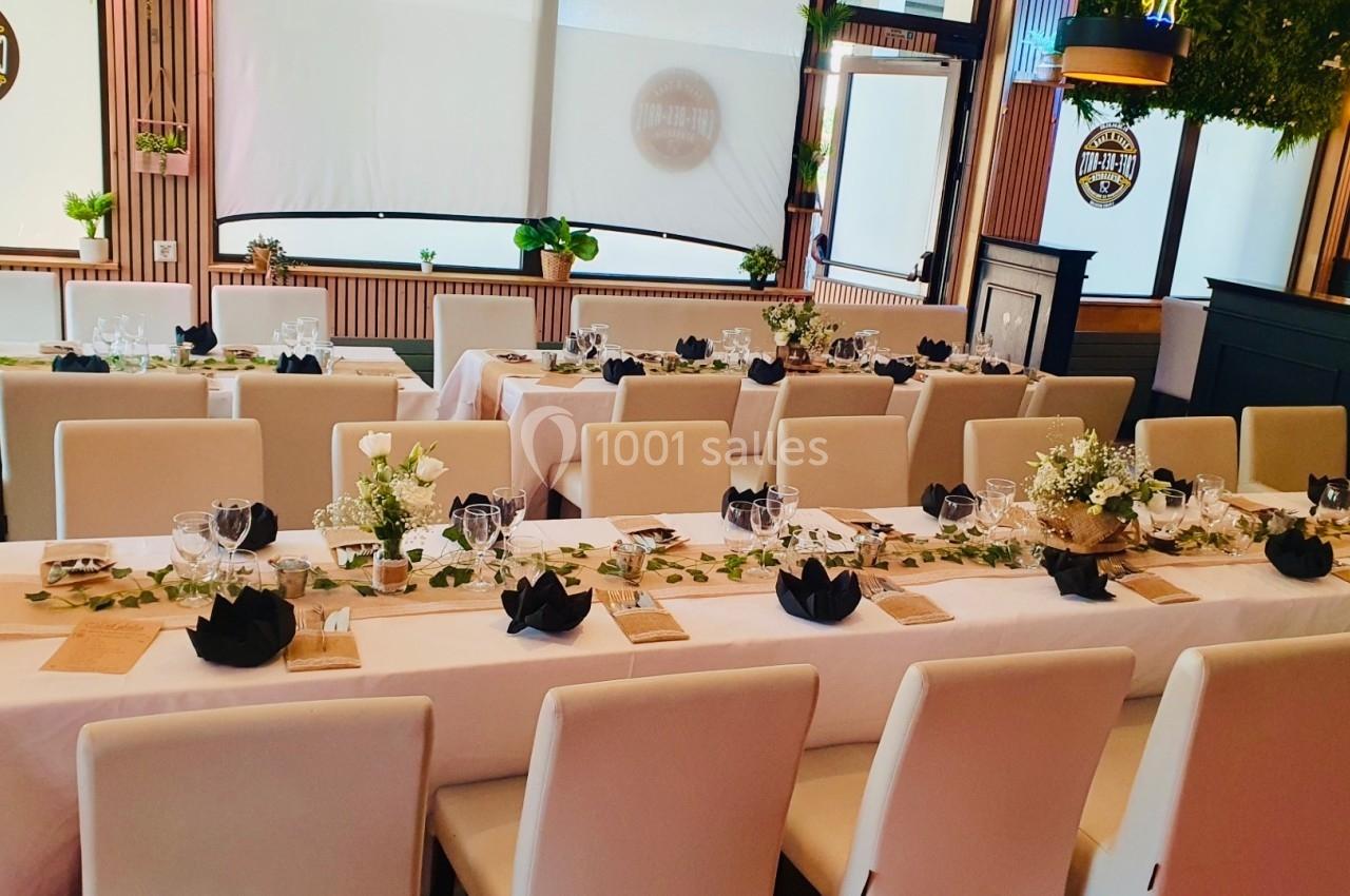 Salle de réception décorée avec des tables dressées, nappes blanches, serviettes noires pliées et arrangements floraux.