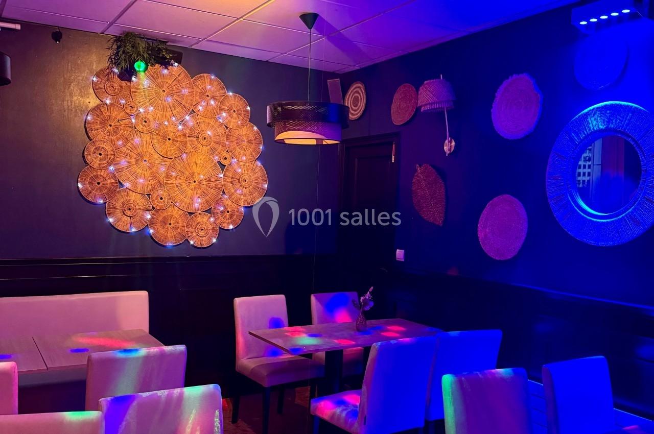 Salle de restaurant avec tables, chaises et décorations murales, éclairée par des lumières colorées.