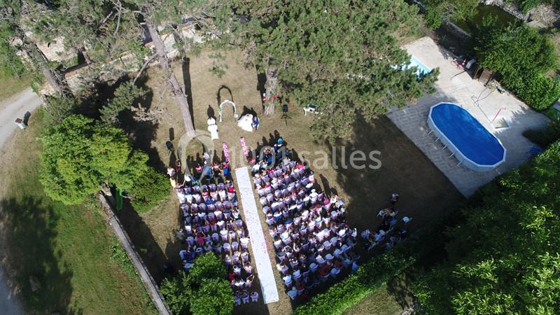 Vue aérienne d'une cérémonie en plein air avec des invités assis, une allée centrale et une piscine à proximité.