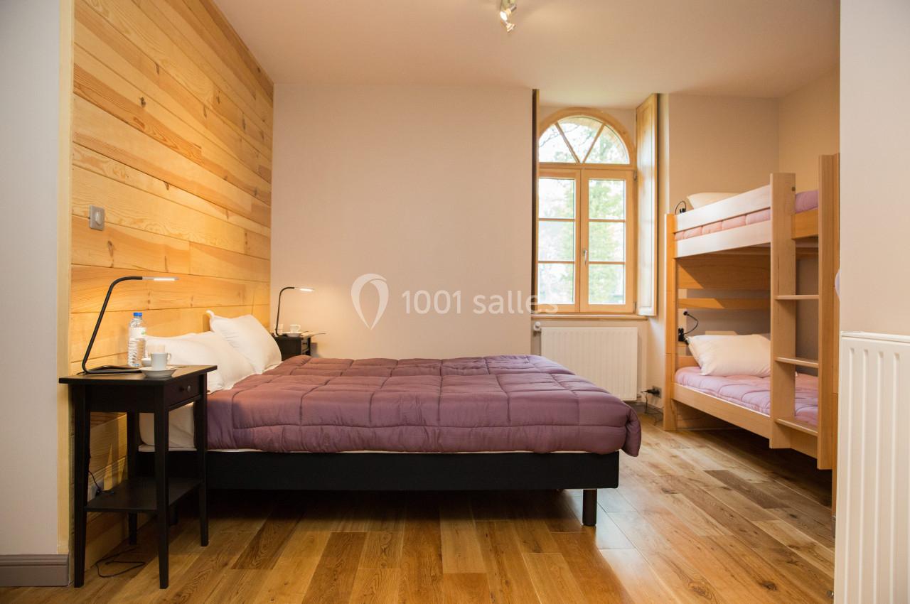 Chambre avec un lit double, des lits superposés, parquet en bois, mur en lambris et fenêtre cintrée.