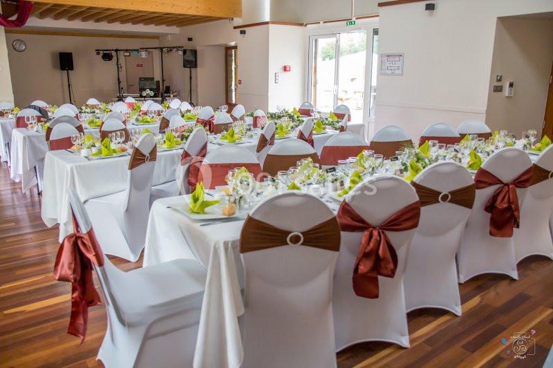 Salle de réception décorée avec des tables dressées, nappes blanches et chaises ornées de nœuds marron.