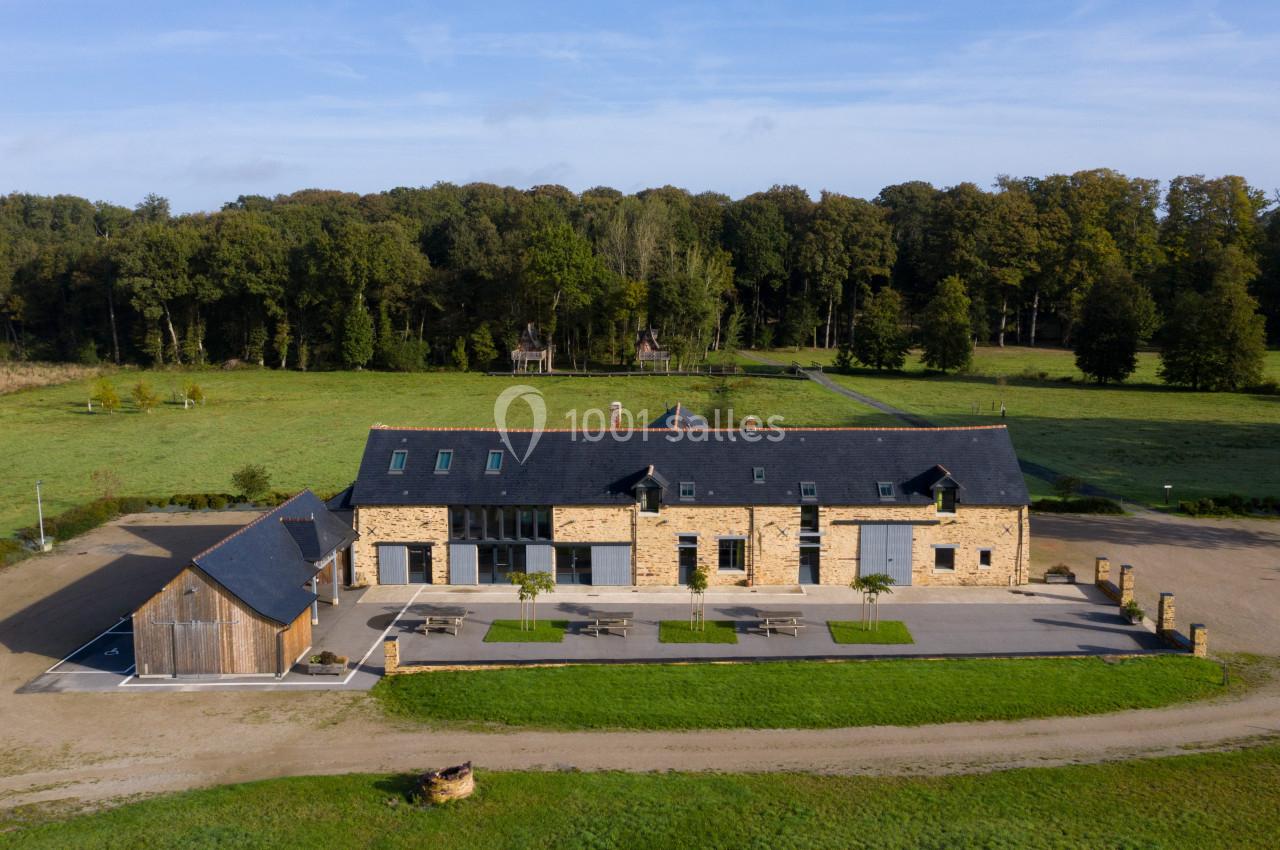 Bâtiment en pierre rénové avec toit en ardoise, entouré de pelouses et d'arbres, sous un ciel dégagé.
