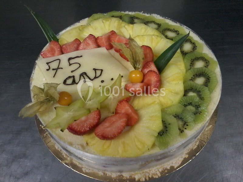 Gâteau décoré de fruits frais (kiwis, fraises, ananas) avec une plaque en chocolat indiquant ’75 ans’.