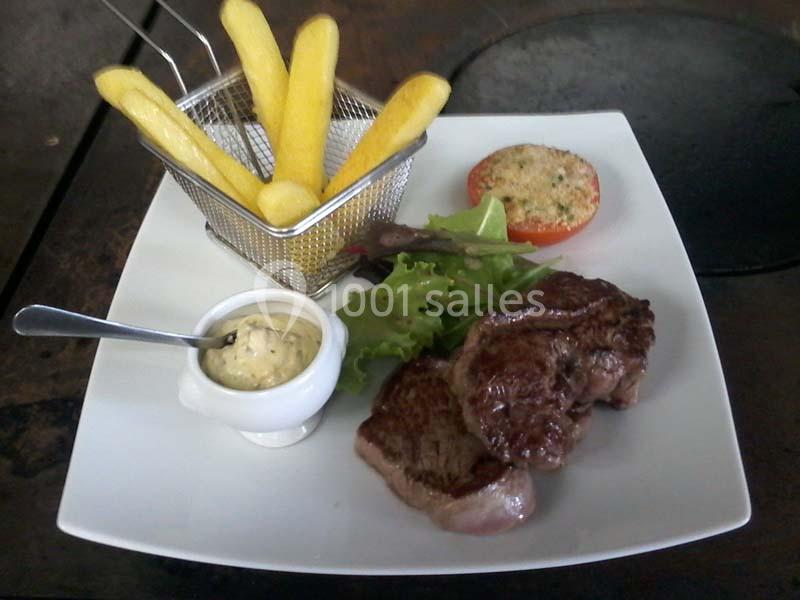 Assiette contenant un steak grillé, des frites dans une petite corbeille, une sauce, une salade et une tomate gratinée.