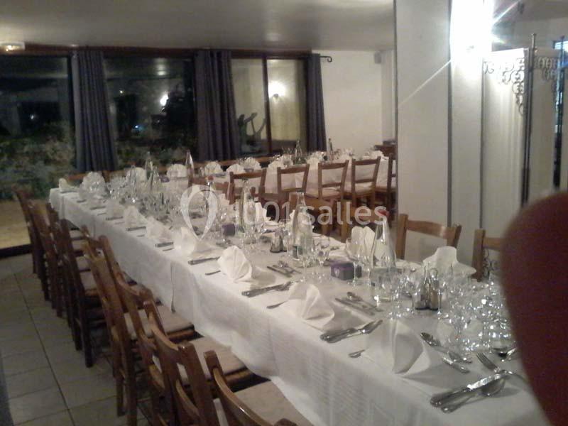 Salle de réception avec longues tables dressées, nappes blanches, verres et couverts, prête pour un repas collectif.