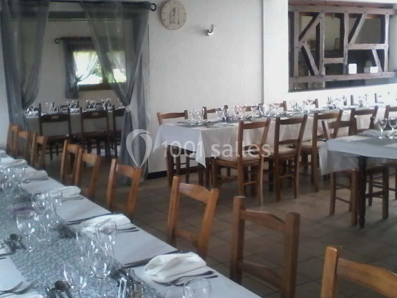 Salle de restaurant avec tables en bois dressées, nappes blanches et vaisselle, ambiance lumineuse et sobre.