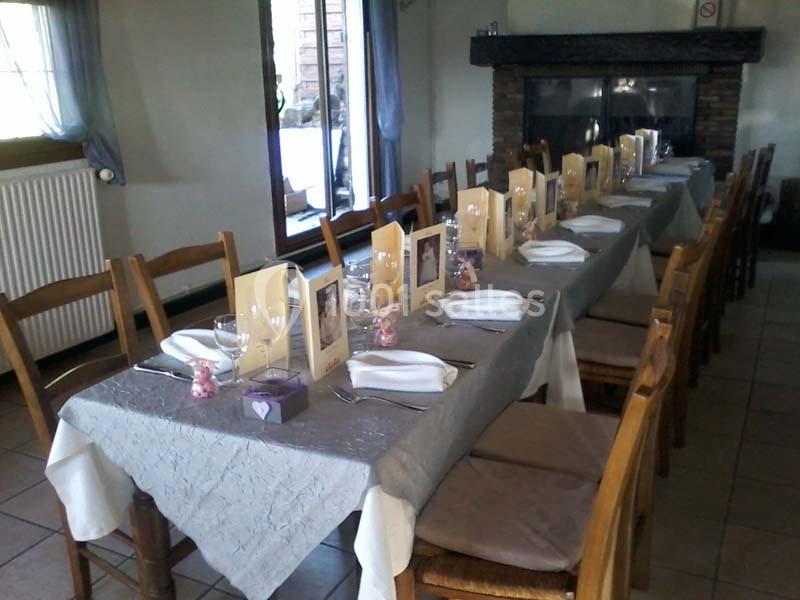Table dressée avec nappes grises, serviettes blanches, menus et décorations, dans une salle avec cheminée en arrière-plan.