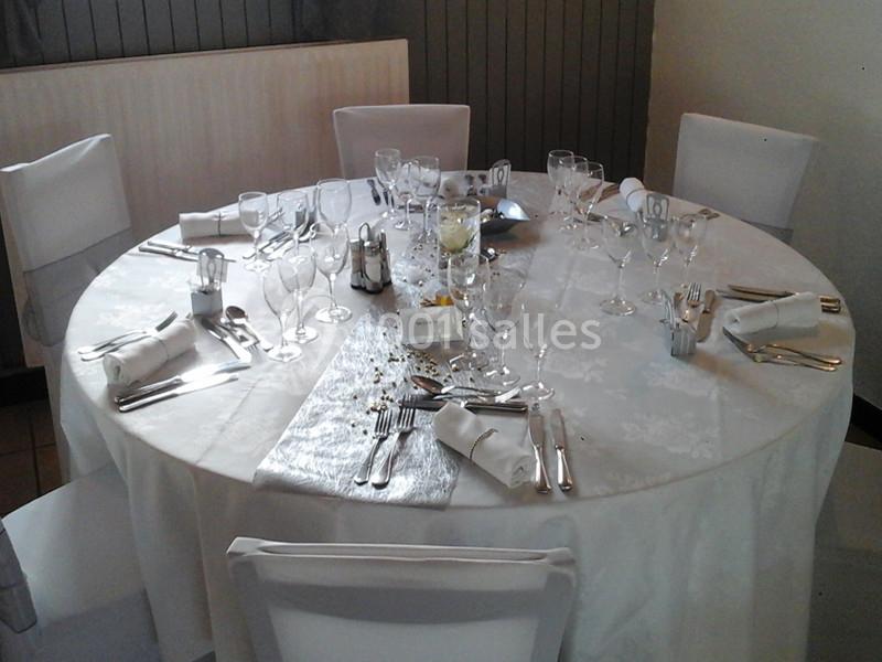 Table ronde élégamment dressée avec nappe blanche, couverts, verres, serviettes pliées et décoration florale centrale.