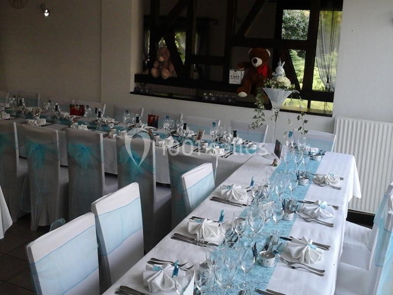 Salle de réception décorée avec des tables dressées, nappes blanches et accents bleu clair, peluches en arrière-plan.