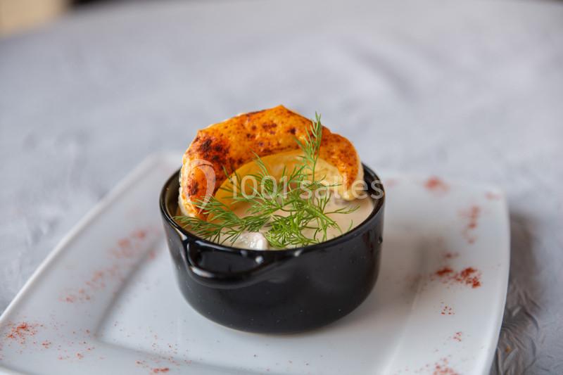 Petit plat noir contenant une crème garnie d'une herbe fraîche et d'un morceau de crustacé grillé.