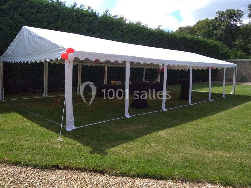 Tente blanche installée sur une pelouse, avec des tables noires dessous et des ballons rouges en décoration.