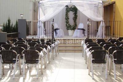 Cour extérieure avec végétation tropicale, terrasse ensoleillée, murs jaunes et mobilier en bois près d'une pergola.