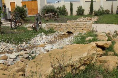 Cour extérieure avec végétation tropicale, terrasse ensoleillée, murs jaunes et mobilier en bois près d'une pergola.