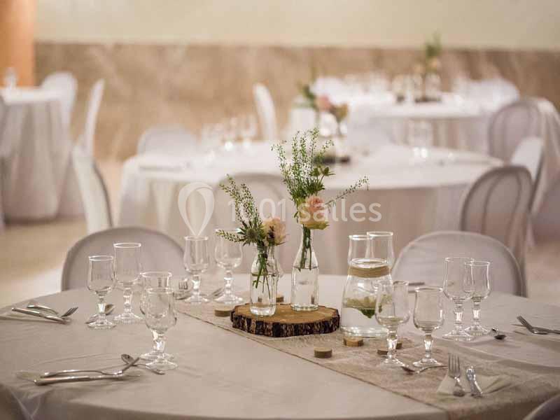 Table dressée avec nappes blanches, verres, couverts et centre de table floral dans une salle de réception.