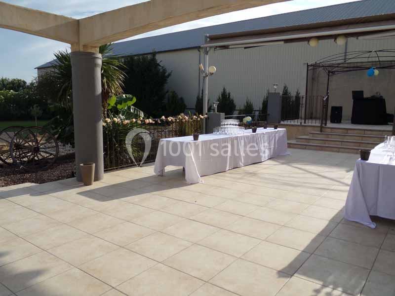 Terrasse extérieure avec tables dressées, pergola, plantes et décor rustique en arrière-plan.